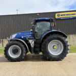 Blue New Holland tractor parked in front of a gray building with a yellow New Holland Agriculture sign