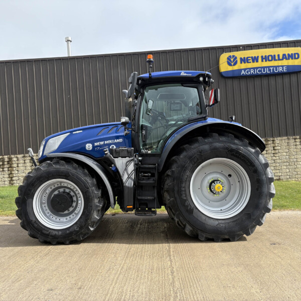Blue New Holland tractor parked in front of a gray building with a yellow New Holland Agriculture sign
