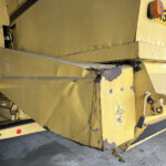 Close-up of yellow industrial machinery with worn paint, rust spots, and a safety sticker near a step edge.