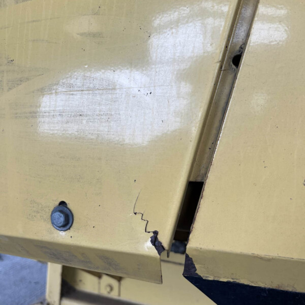 Close-up of a chipped yellow metal panel with a curved metal strip and a hole, showing wear and damage