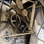 Close-up of dusty yellow industrial machinery showing belts and pulleys inside a frame, with grime and exposed components.