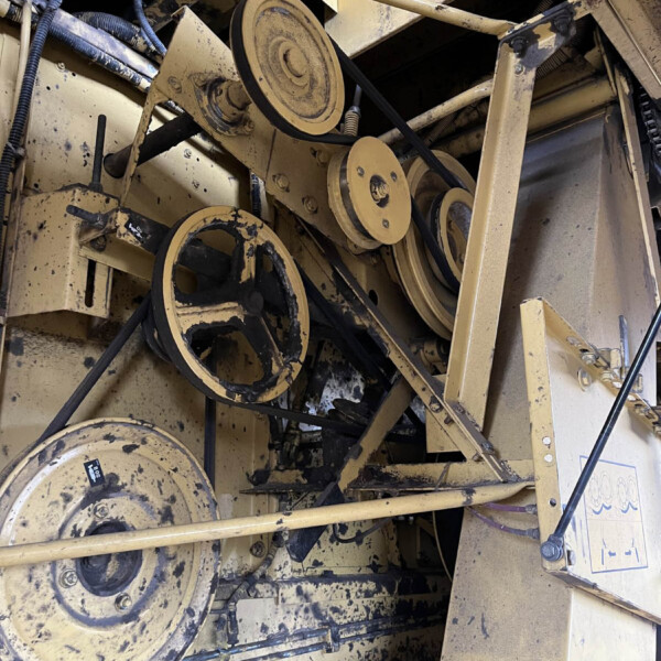 Close-up of dusty yellow industrial machinery showing belts and pulleys inside a frame, with grime and exposed components.