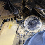 Close-up of dusty yellow industrial machinery showing chains, gears, and hoses with worn, dirty surfaces.