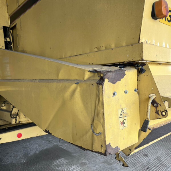 Close-up of yellow industrial machinery with worn paint, rust spots, and a safety sticker near a step edge.