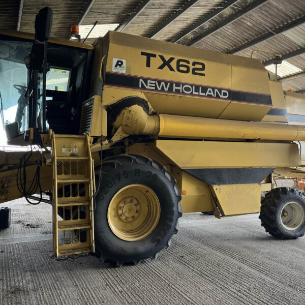 New Holland TX62 combine harvester parked inside a shed with corrugated metal roof.