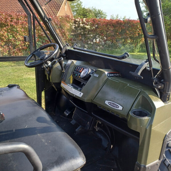 Interior of a green Ranger off-road vehicle showing steering wheel, dashboard, and rugged controls outdoors.