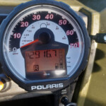 Close-up of a Polaris ATV/UTV instrument cluster showing an analog speedometer (0–70 mph) with red numbers and a small digital display below.
