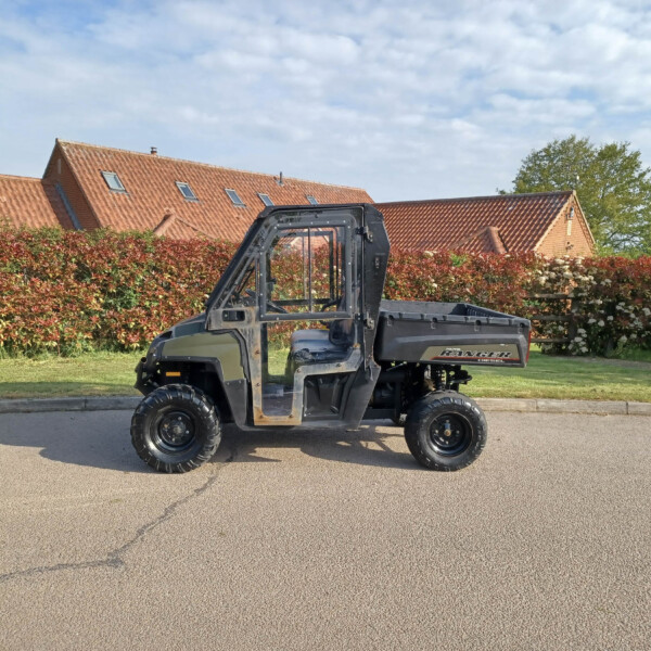 Polaris Ranger Diesel UTV parked on a street with red-tiled houses and a hedge in the background.