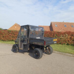 Black Polaris Ranger Diesel utility vehicle parked on a residential street with red hedges and brick houses in the background.