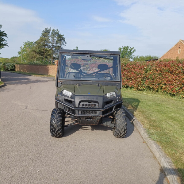 Front view of a dark gray Polaris off-road utility vehicle parked on a suburban street with a hedge and brick house in the background