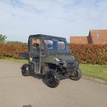Black utility side-by-side ATV with a roll cage parked on a residential street, red hedge and red-tiled house in the background.