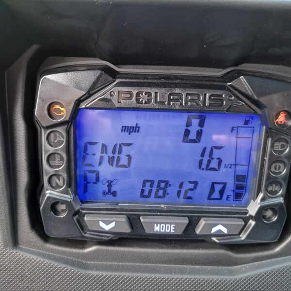 Close-up of a Polaris ATV instrument panel with blue backlit display showing speed 0 mph and warning icons on the sides.