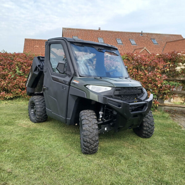 Polaris off-road side-by-side parked on a lawn with a hedge and red-tiled houses in the background.