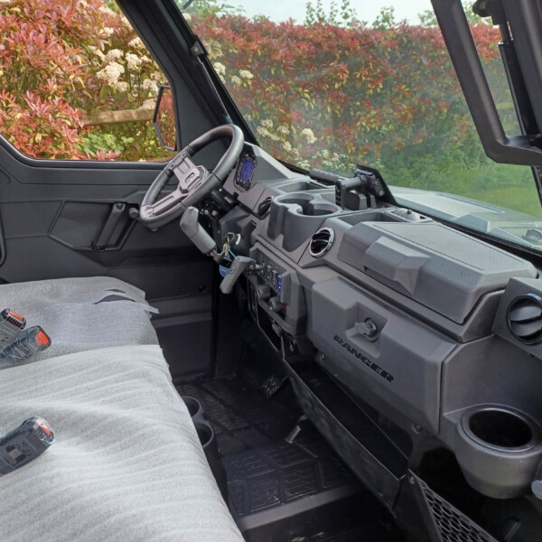 Interior of a pickup truck cab with a gray fabric seat, steering wheel, and dashboard; hedge visible through the windows outside.