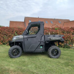 Black utility off-road vehicle (Ranger) parked on a grassy lawn with a red hedge and red-tiled houses in the background.