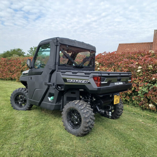 Polaris Ranger off-road utility vehicle parked on a grassy lawn beside a red-leaf hedge and a tiled roof house nearby.