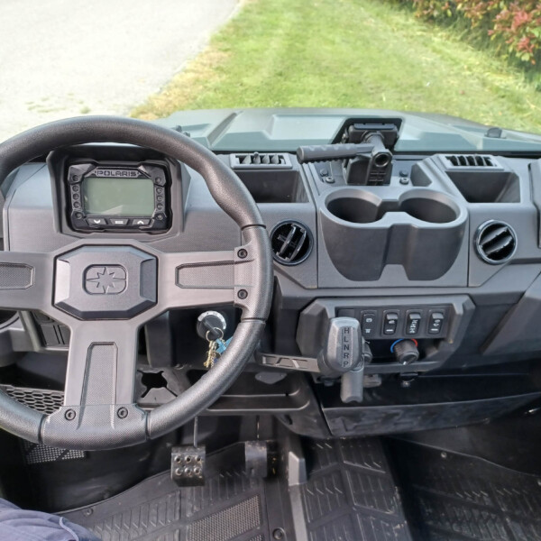 Driver's cockpit of a Polaris utility vehicle with steering wheel, instrument panel, gear shifter, and cup holders visible