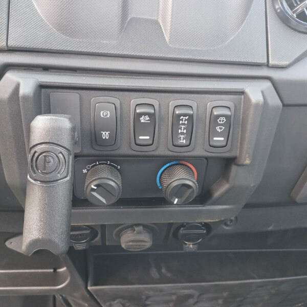 Close-up of the lower dashboard with four rocker switches (parking brake, a vehicle function icon, axle/drivetrain icon, and windshield/wiper icon) and climate control dials below showing blue and red temperature marks.