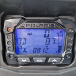 Digital instrument cluster showing speedometer at 0 mph on a Polaris gauge, with warning icon illuminated on the left and fuel gauge on the right.