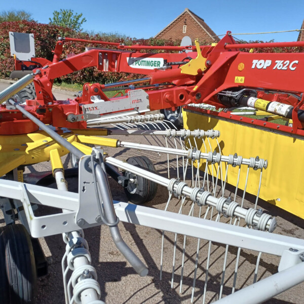 Close-up of a red and yellow farm implement with tines and springs mounted on a trailer, parked on a driveway.