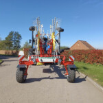 Front view of a large red Pottinger agricultural implement with folding tines on a driveway.