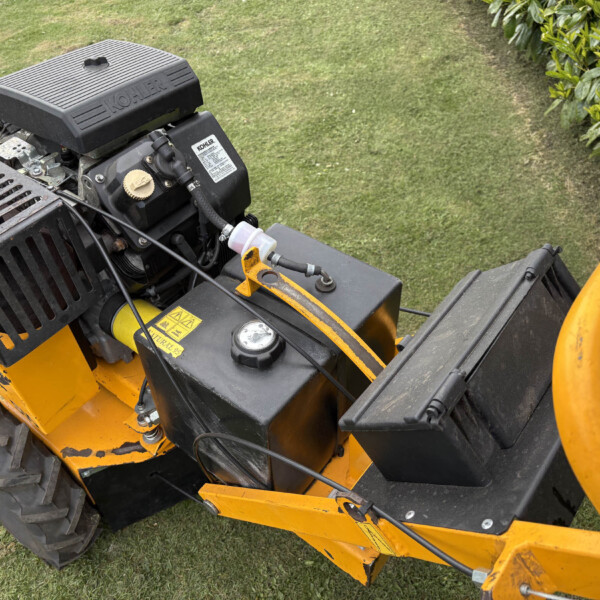 Close-up of a small gasoline engine on a yellow lawn mower, with a black air cover, fuel cap, and hoses visible on grass.