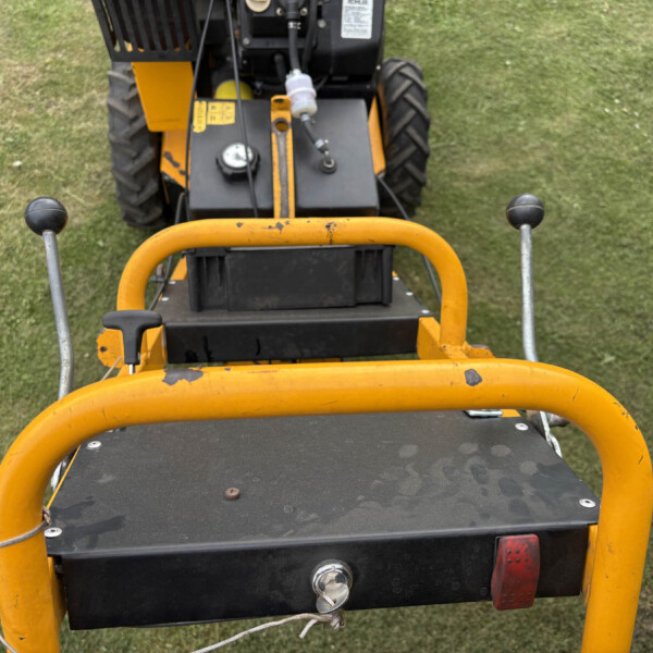 Top-down view of a yellow industrial machine's cockpit with black controls on grass surface.]','