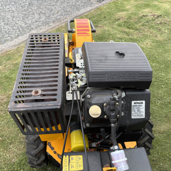 Front view of a yellow construction machine with a KOHLER engine cover and vented metal guard, on grass nearby.