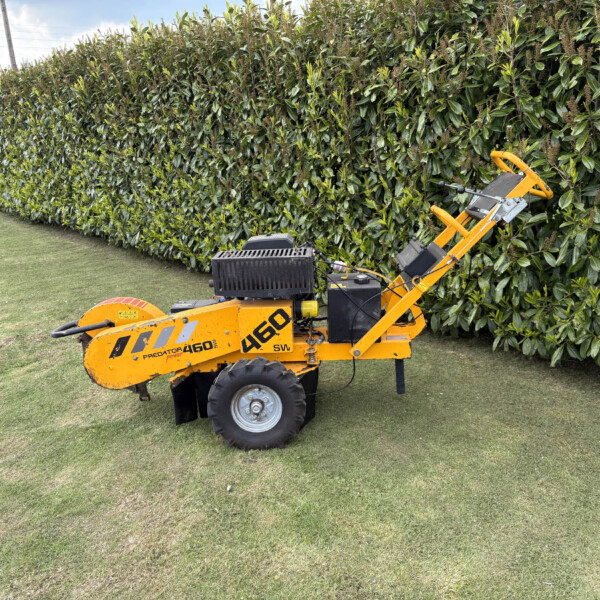 Yellow hedge-trimming machine parked beside a dense green hedge along a grassy area.