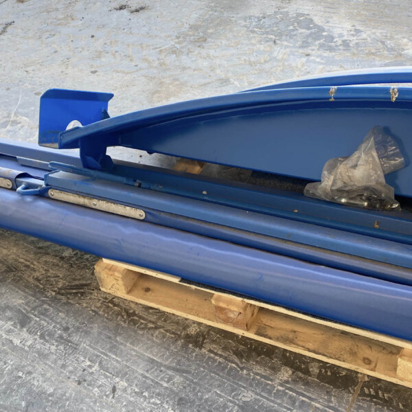 Blue metal duct sections stacked on a wooden pallet in a workshop/warehouse floor, with plastic bags tucked inside one duct.