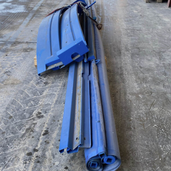 Blue industrial straps rolled up with metal hardware placed on a dusty concrete floor at a construction site placeholding materials nearby.
