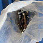 Plastic bag filled with assorted metal bolts, nuts, and washers on a blue surface (construction hardware).