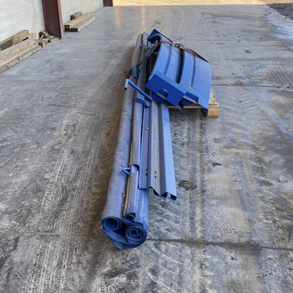 Blue metal beams and rolled blue tarps strapped on a pallet in an outdoor industrial yard near a warehouse door.