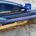 Stack of blue-painted metal beams and brackets on a wooden pallet in a workshop or construction area.