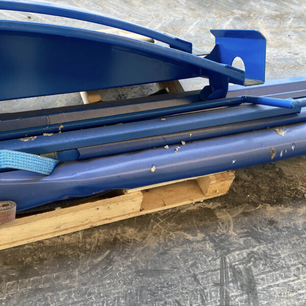 Stack of blue-painted metal beams and brackets on a wooden pallet in a workshop or construction area.