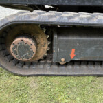 Close-up of a muddy tracked vehicle wheel and rubber track, with an orange arrow sticker on the side panel.