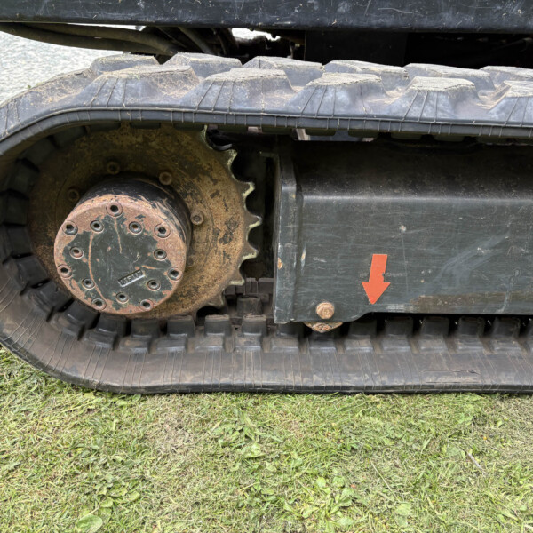 Close-up of a muddy tracked vehicle wheel and rubber track, with an orange arrow sticker on the side panel.