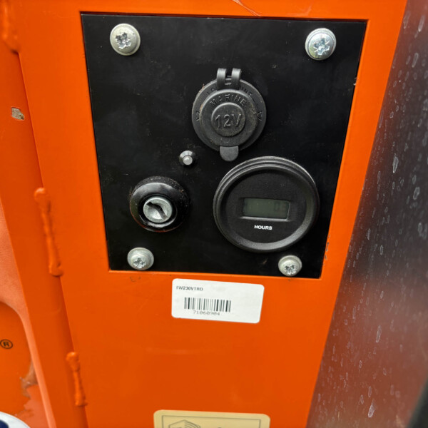 Close-up of an orange machinery control panel with a round 12V marine power outlet, screws, and an hour meter nearby