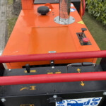 Close-up of an orange industrial machine deck with a black knob, warning label, and red rollers