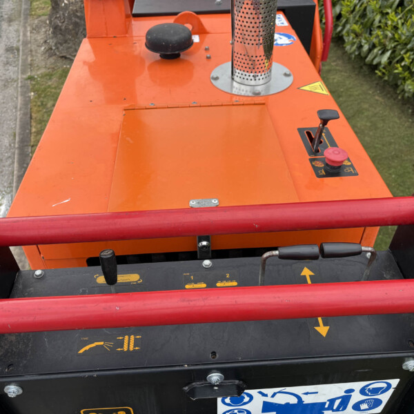 Close-up of an orange industrial machine deck with a black knob, warning label, and red rollers