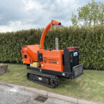 Orange Timberwolf TW 230VTR stump grinder on tracks beside a hedge by the roadside.