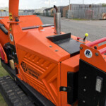 Orange Timberwolf wood processor on tracks with exhaust stack and safety labels in a storage yard.