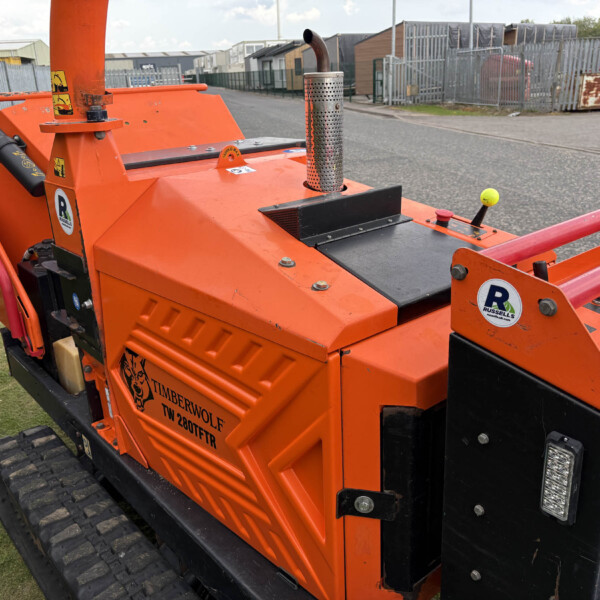 Orange Timberwolf wood processor on tracks with exhaust stack and safety labels in a storage yard.