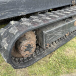Close-up of a muddy tracked vehicle wheel and rubber tread with rusted metal components on grass surface