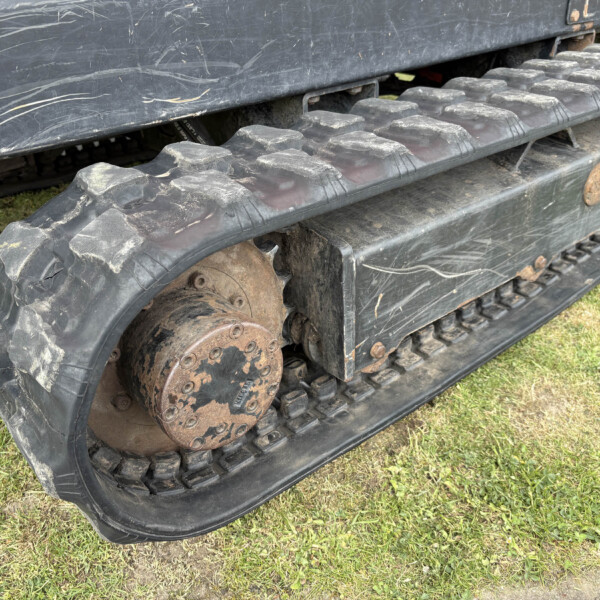 Close-up of a muddy tracked vehicle wheel and rubber tread with rusted metal components on grass surface