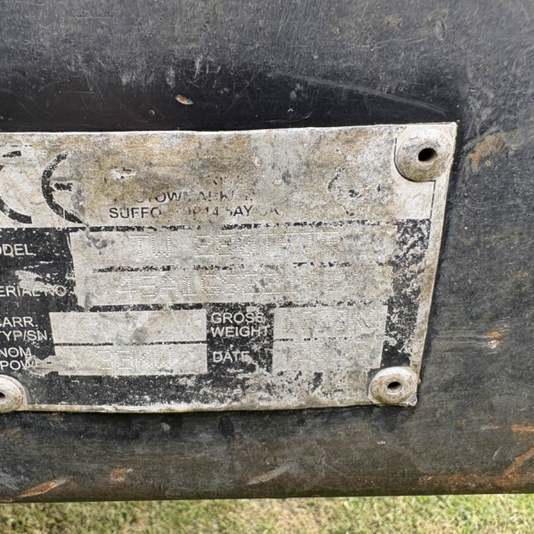 Close-up of a weathered metal nameplate mounted with four screws on a dark, dirty surface; most text is faded and illegible.