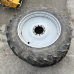 Large off-road tractor tire with a gray metal rim on a concrete surface; a yellow industrial machine is partially visible in the upper left corner.