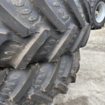 Close-up of a heavy black tractor tread with muddy ruts and circular bolt plates, showing worn industrial rubber tracks in a yard.