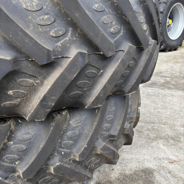 Close-up of a heavy black tractor tread with muddy ruts and circular bolt plates, showing worn industrial rubber tracks in a yard.