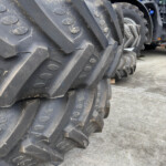Close-up of muddy tractor tires stacked in a yard, with blue tractors visible in the background.